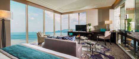 Une chambre d’hôtel avec un grand lit, un canapé, un bureau avec une télévision et une vue sur l’océan.