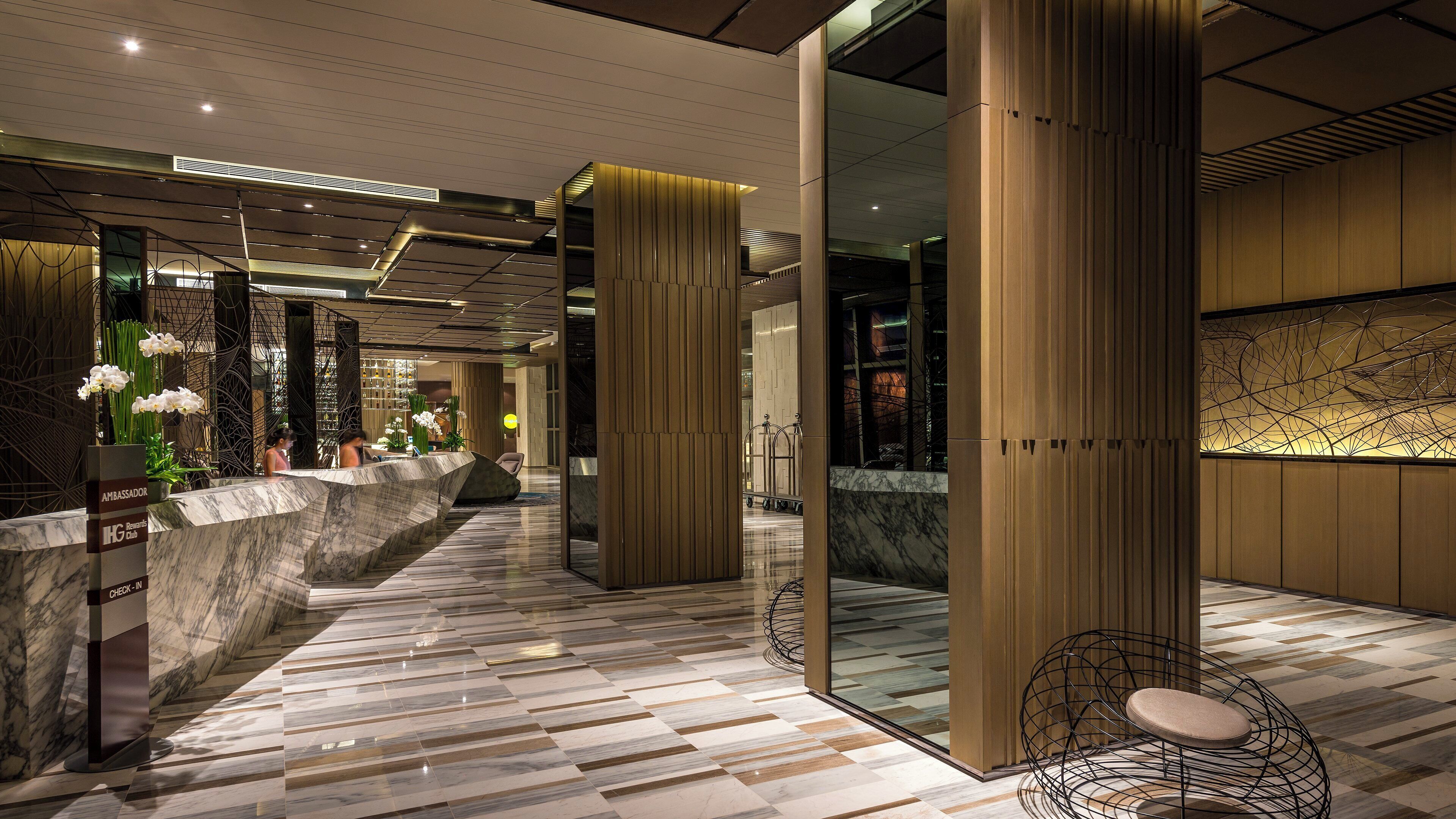 A modern hotel lobby with a marble reception desk, check-in counters, and a seating area with a unique wire chair.