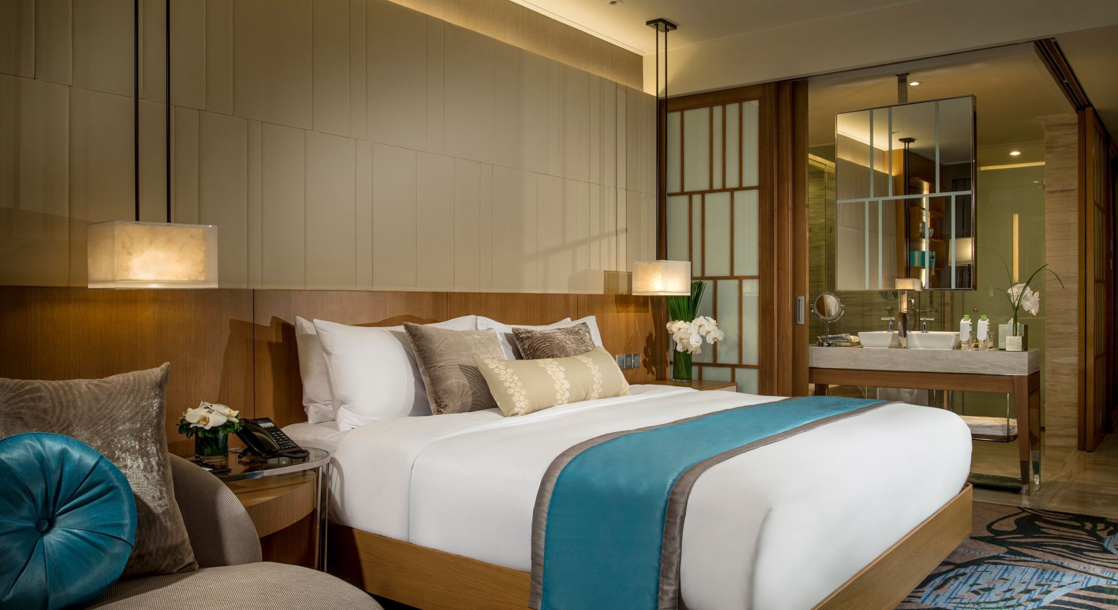 A hotel room with a large bed, bedside tables, a desk, a mirror, and a bathroom with a sink and mirror.