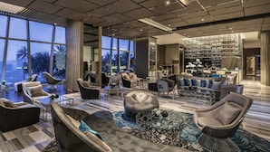 A spacious lounge area with multiple seating options, a bar with a variety of bottles, and large windows offering a view of palm trees. - InterContinental Nha Trang by IHG (Nha Trang)