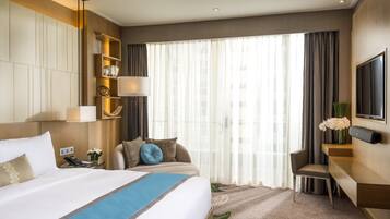 Een hotelkamer met een groot bed, een bureau, een stoel, een televisie en een raam met gordijnen.