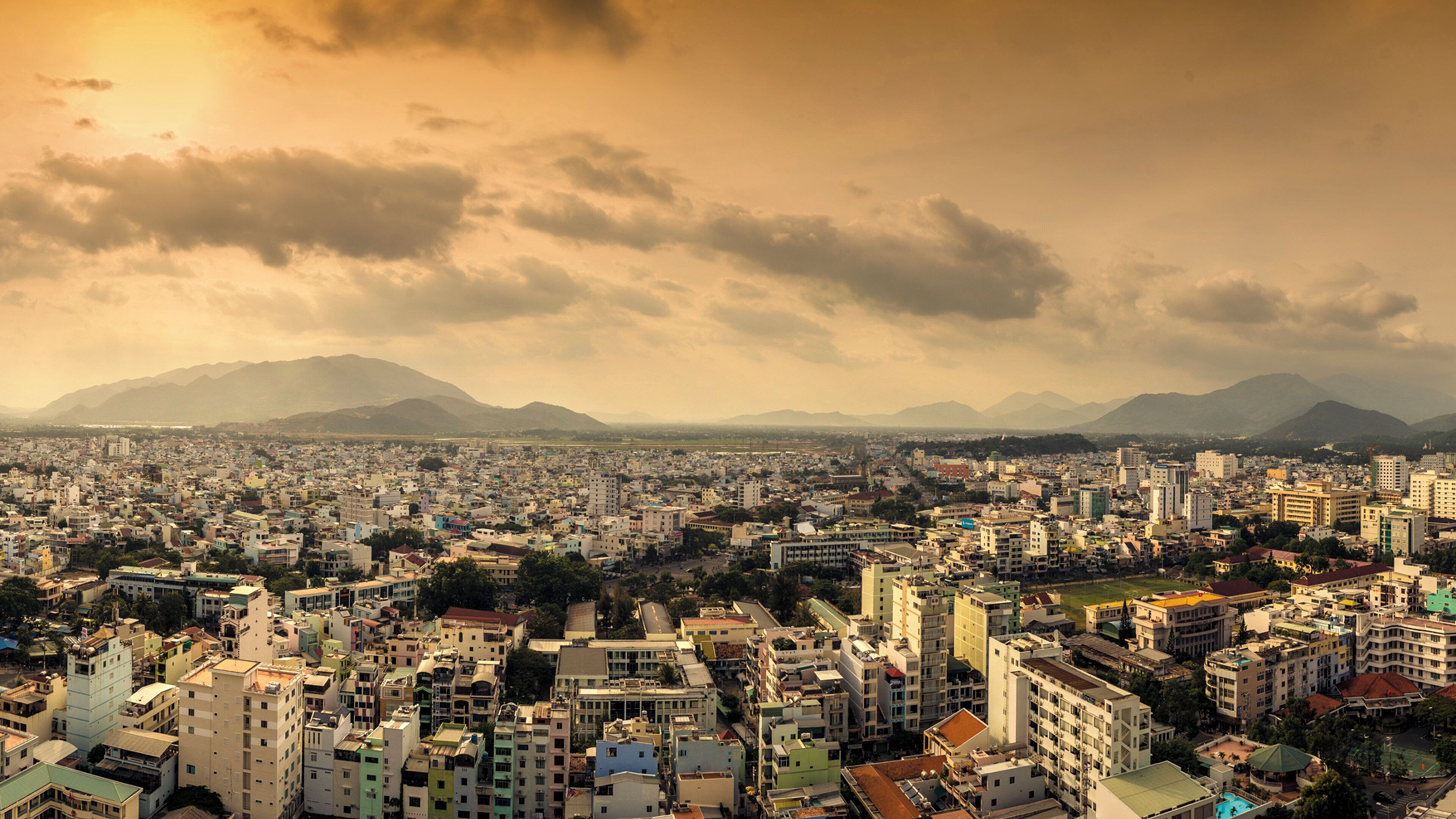 A cityscape with a dense urban area, buildings, and mountains in the background.