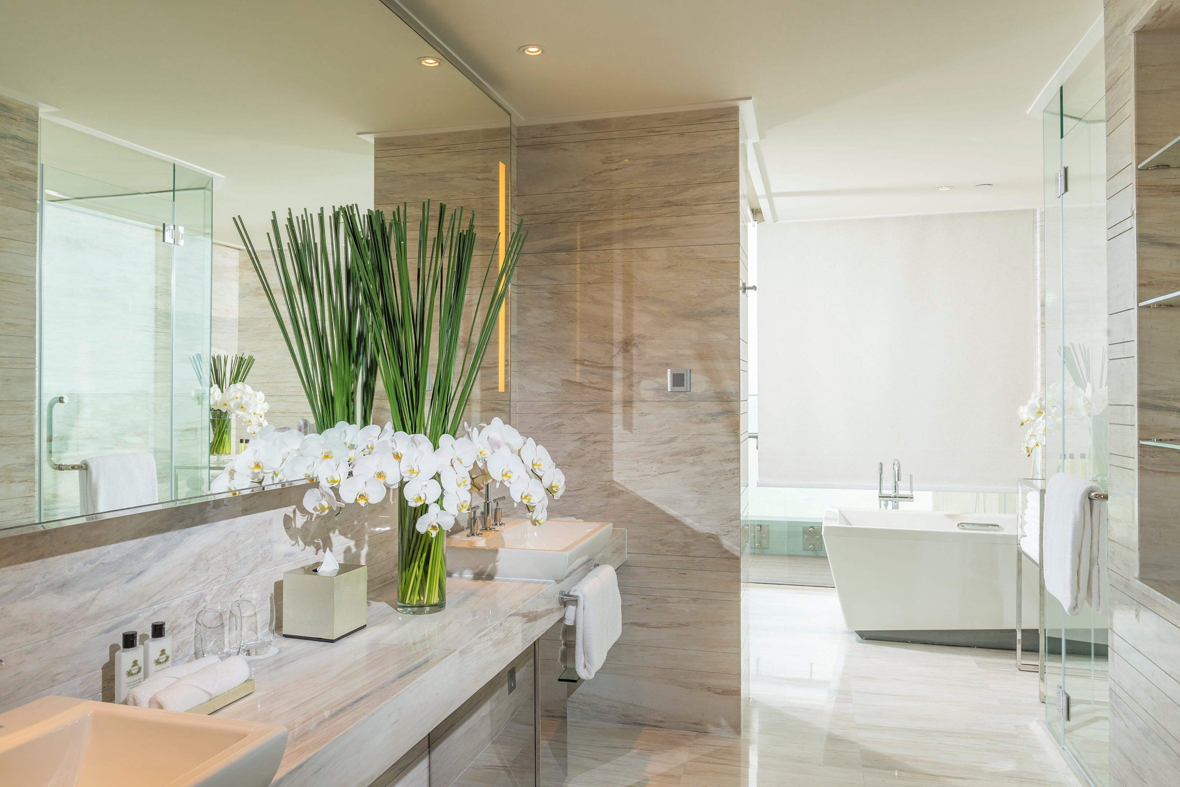 A modern bathroom with a large mirror, two sinks, a bathtub, and decorative orchids.