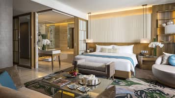 A modern hotel room with a large bed, a sitting area with a coffee table, a glass shower enclosure, and a dining area with a tray of breakfast items.