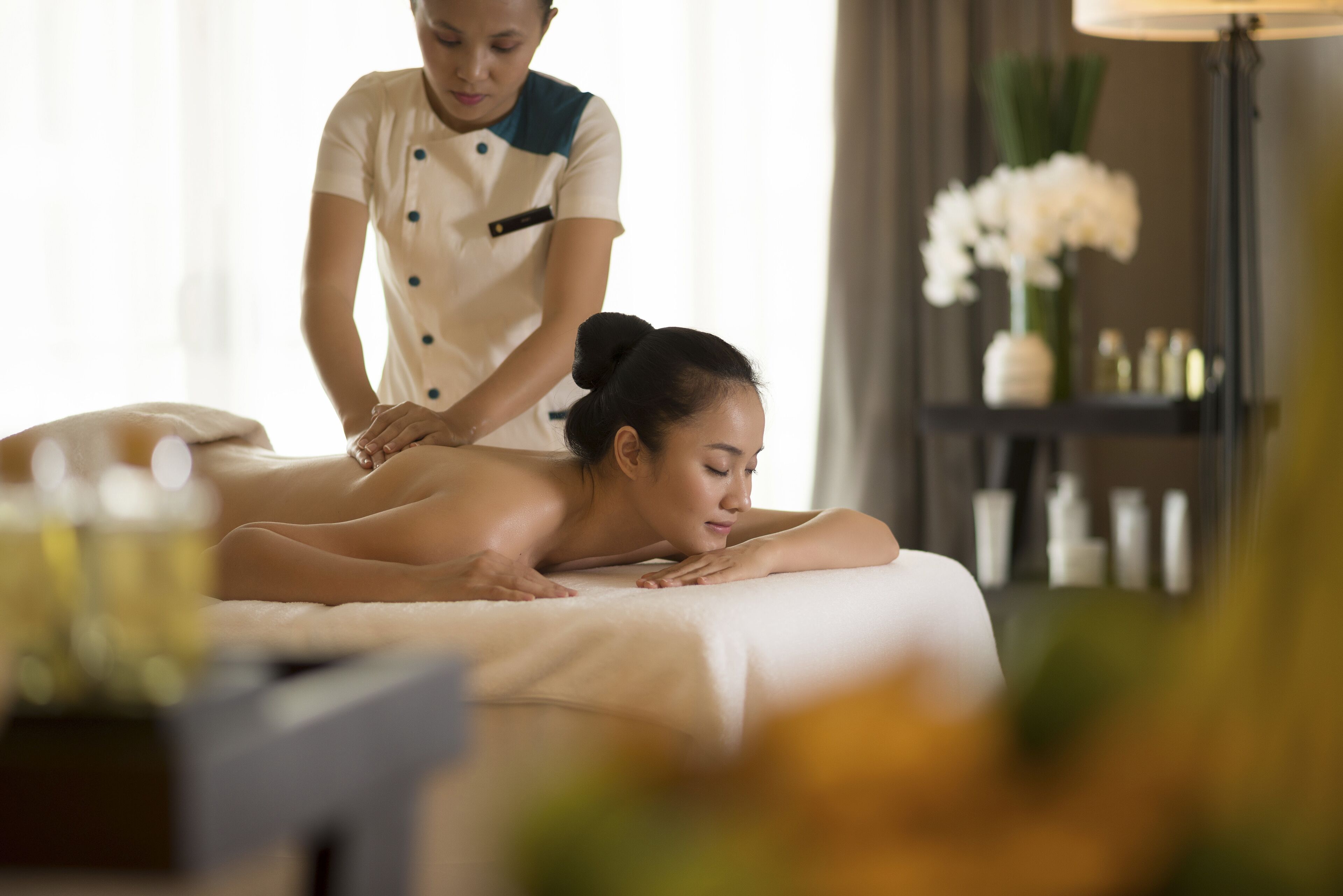 Sesión de masoterapia en un entorno de spa, con una camilla, un terapeuta y un florero decorativo con flores.