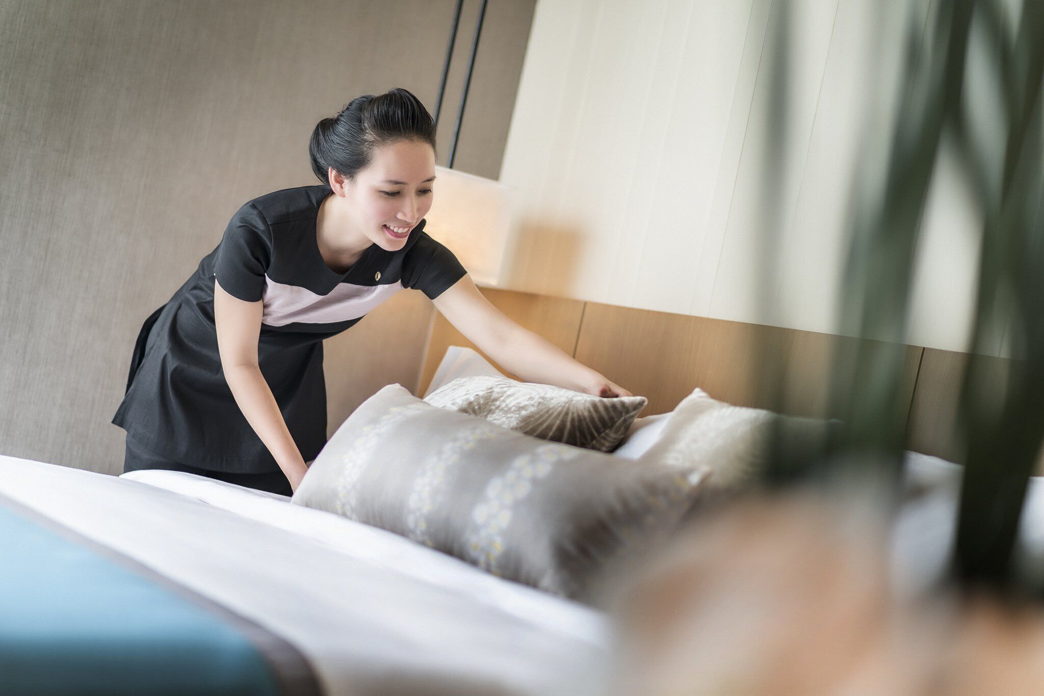 A person adjusting a bed in a room with a modern design, including a wooden headboard and a visible plant.