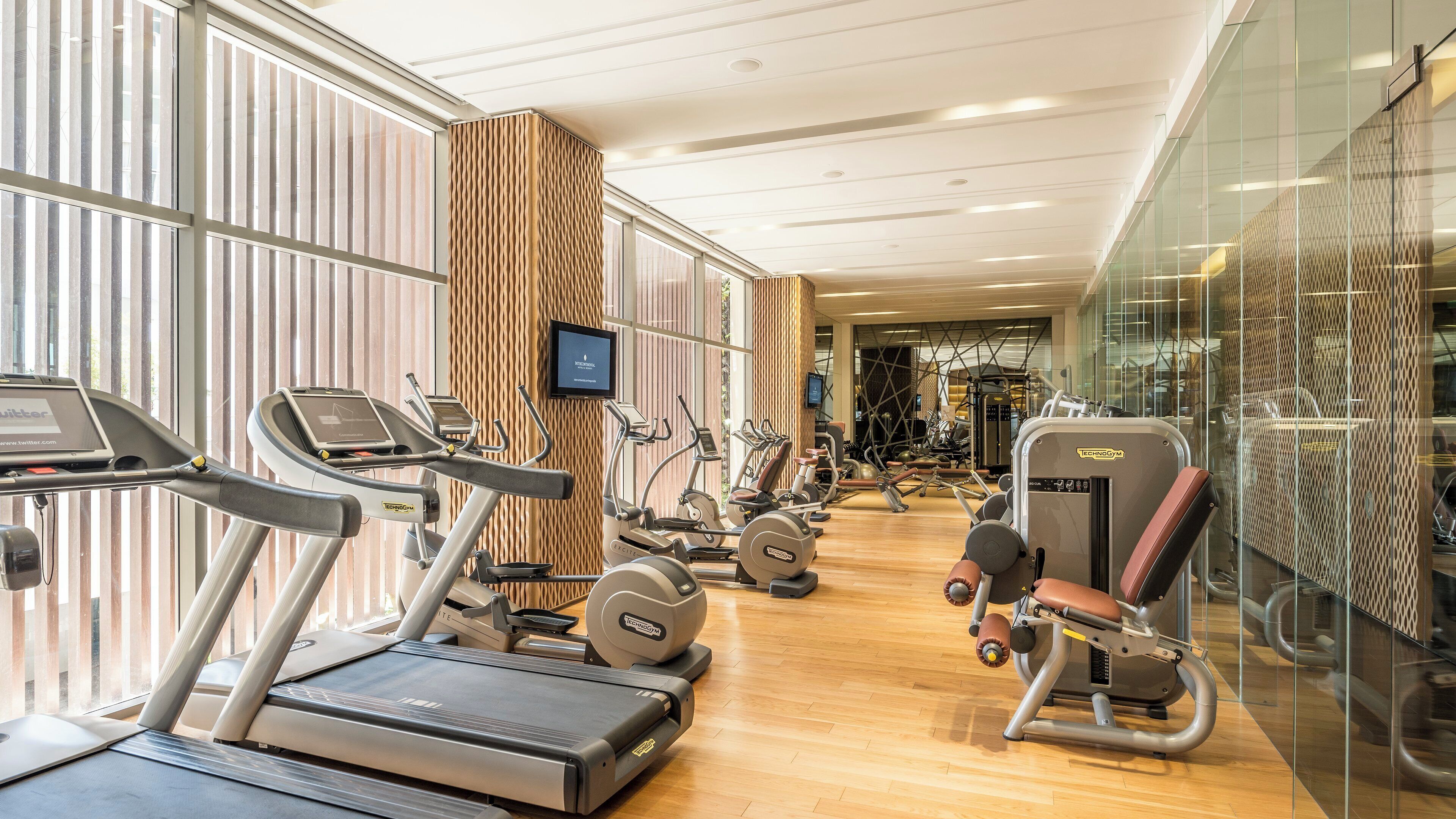 A modern gym with treadmills, elliptical machines, and weight equipment.