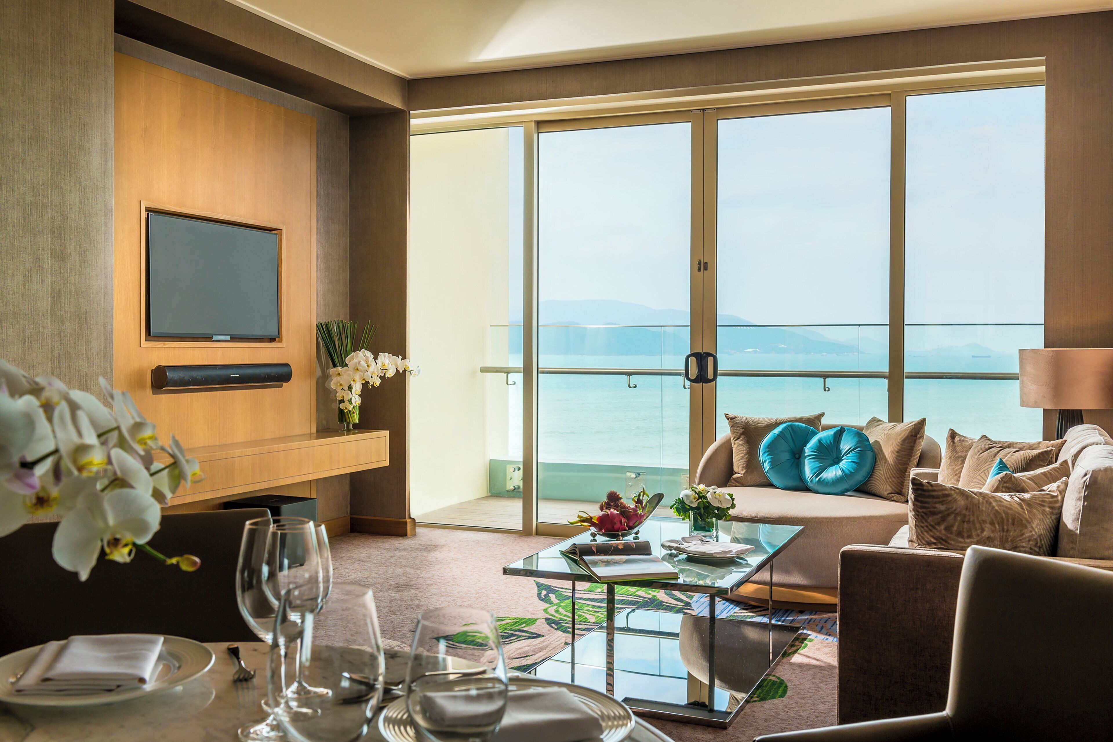 Une chambre d’hôtel avec un balcon, une télévision, une table à manger et un canapé agrémenté de coussins décoratifs.