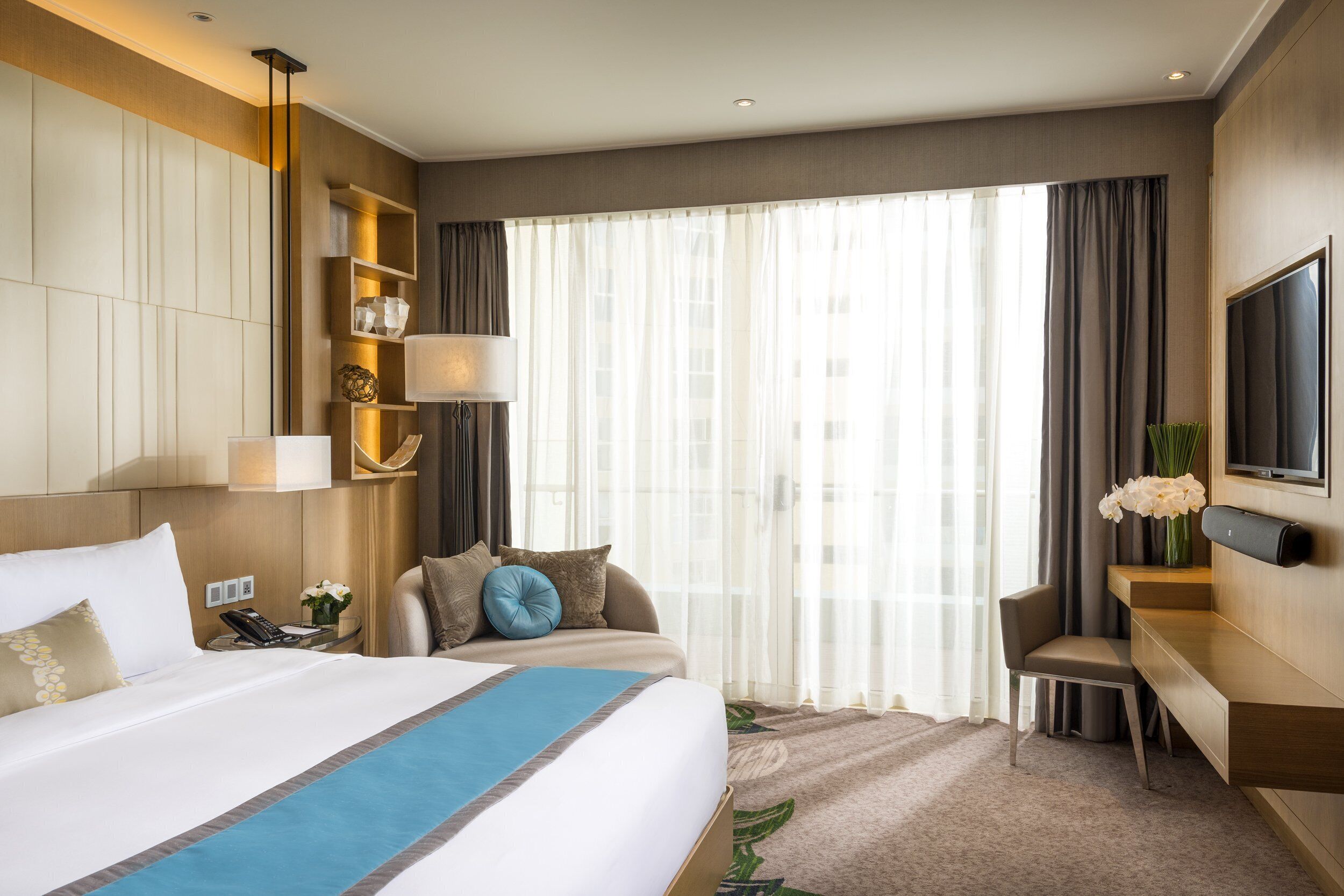 Une chambre d’hôtel avec un grand lit, un bureau, une chaise, une télévision et une fenêtre avec des rideaux.