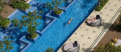 An aerial view of a swimming pool with a person swimming, surrounded by lounge chairs and potted plants.