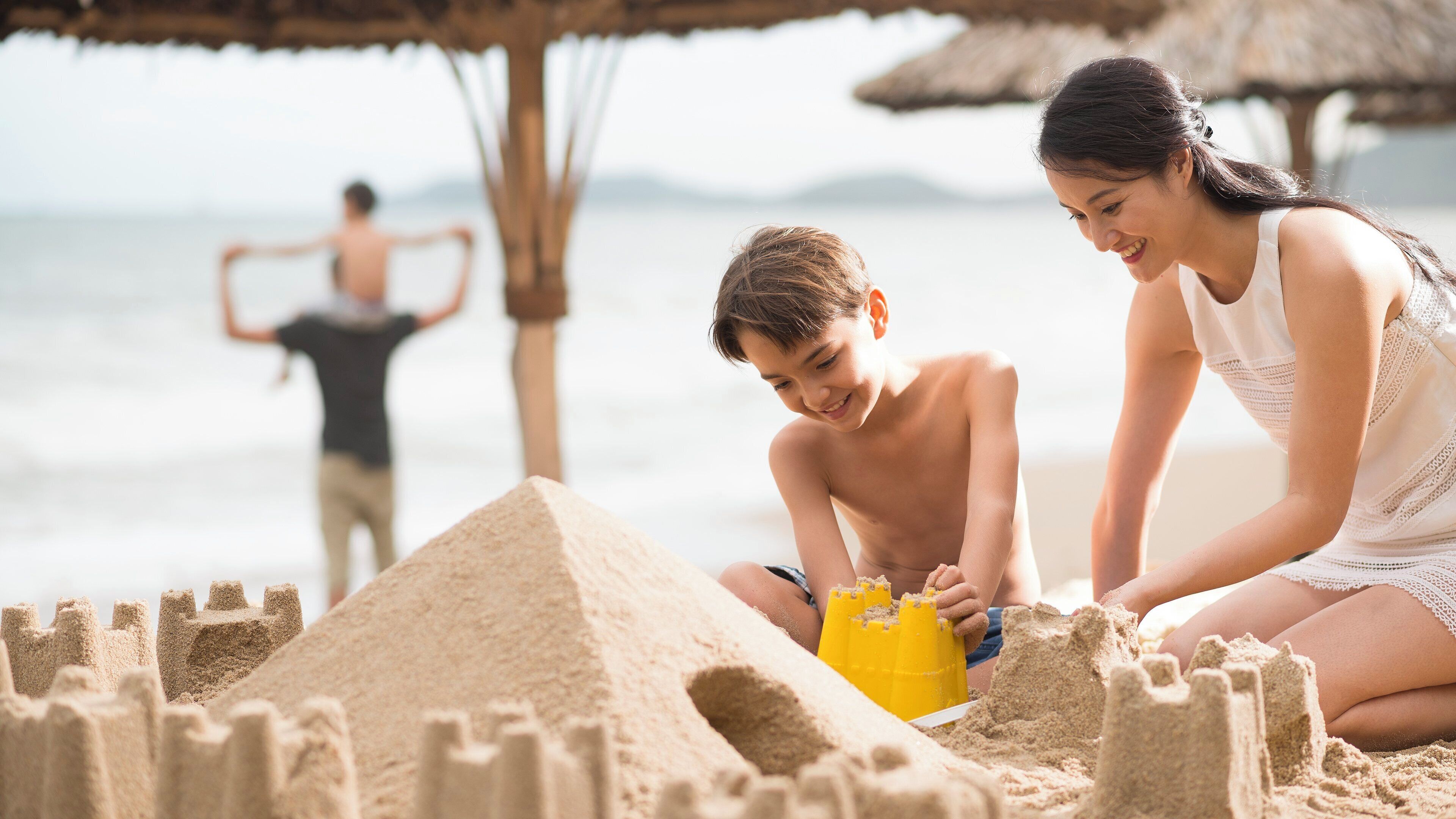 Eine Szene am Strand mit einer Sandburg und einer Person im Vordergrund.