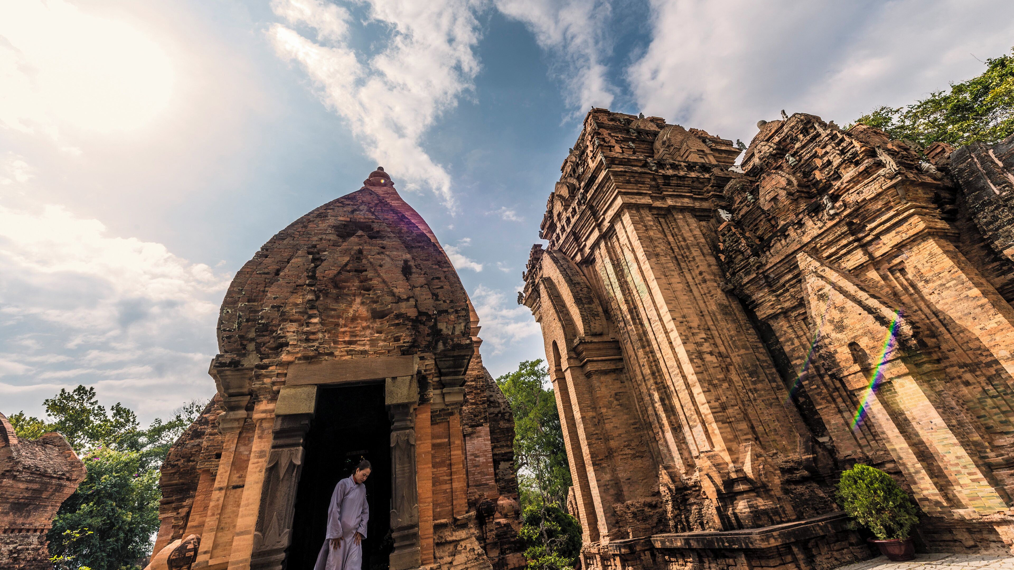 An ancient temple with a large dome and intricate carvings, a person standing at the entrance, and a clear sky.