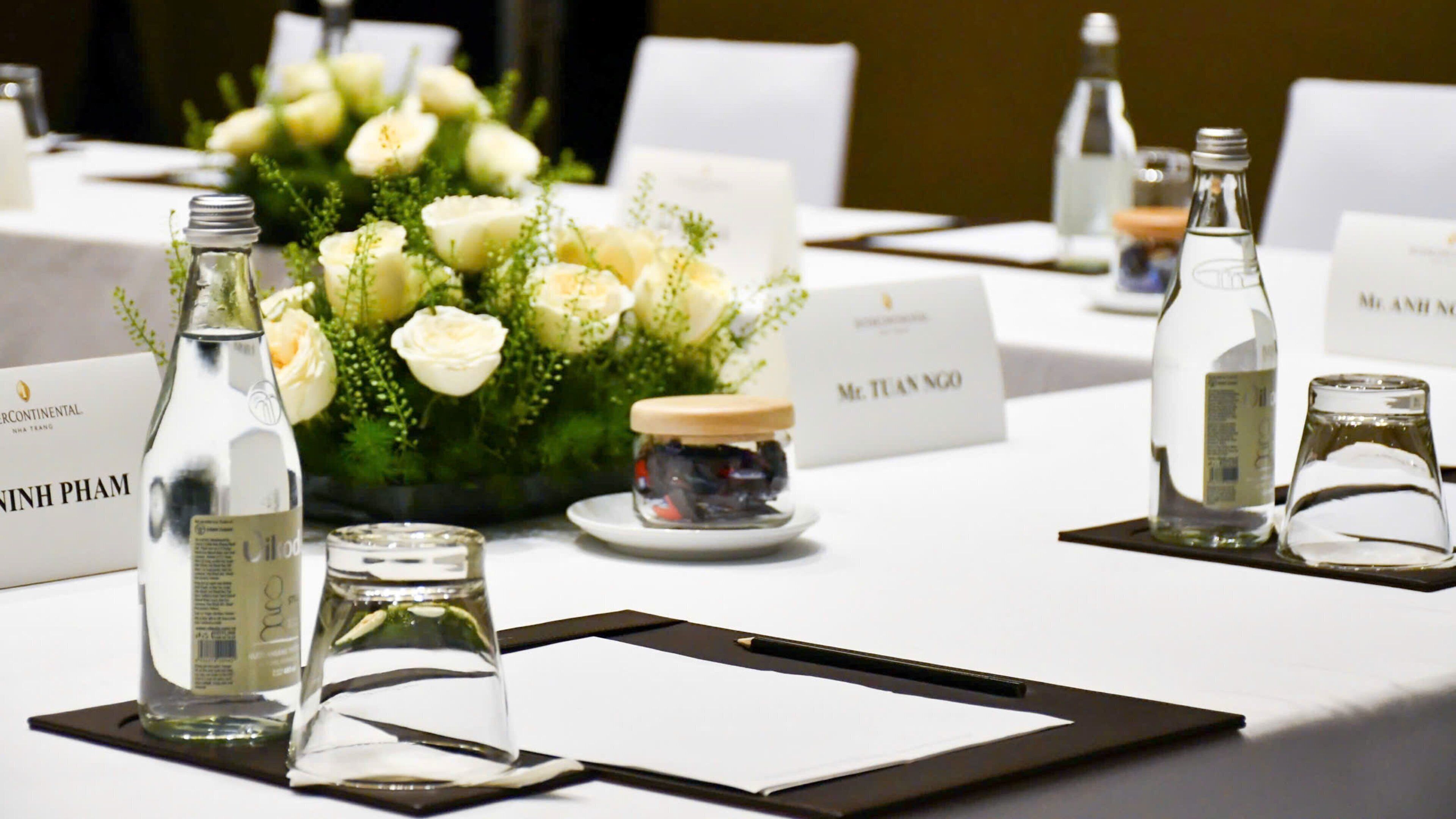 Una mesa de conferencias con tarjetas de identificación, botellas de agua y un frasco pequeño de bocadillos.