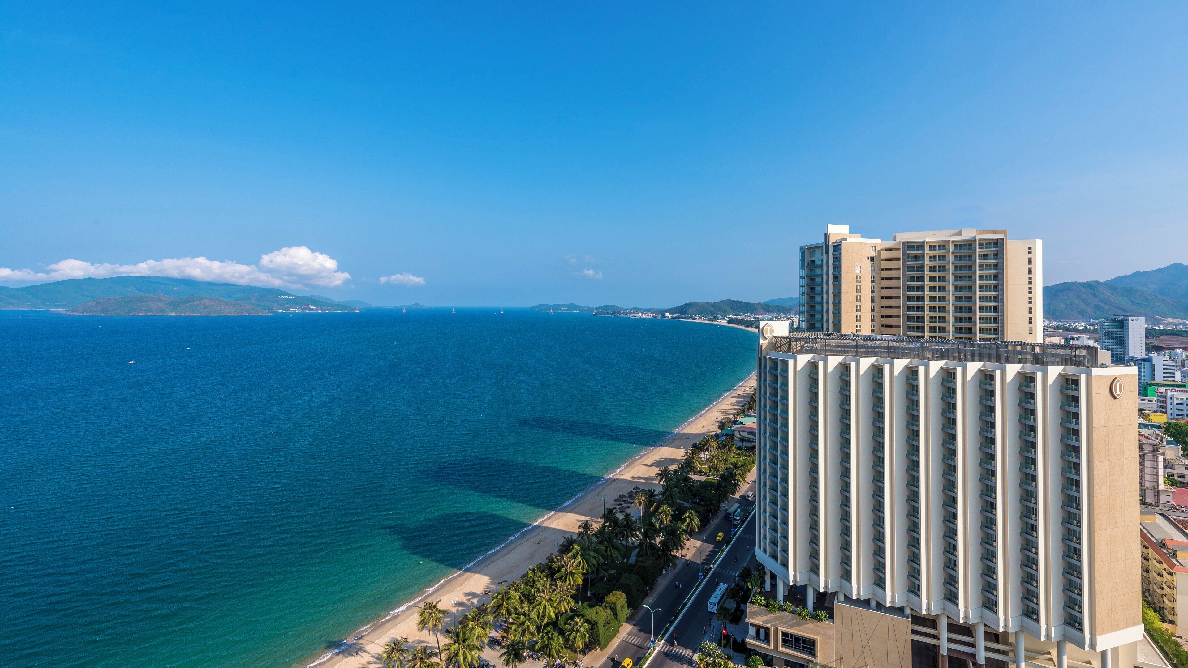 A coastal hotel with a beach view, multiple stories, and a prominent logo on the building.
