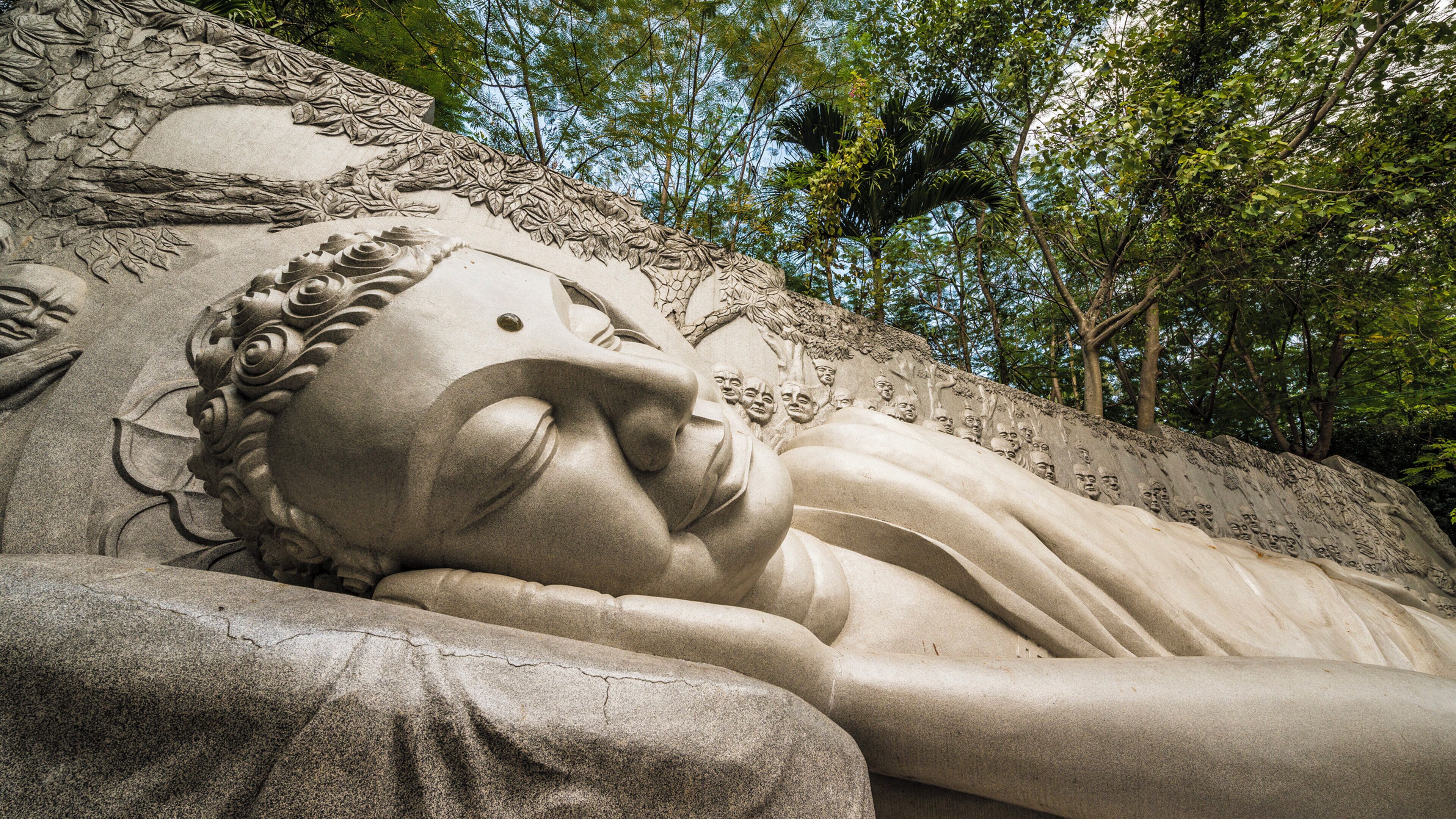 Una gran escultura de pedra d'una figura estesa, amb detalls tallats i envoltada d'arbres.