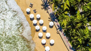 An aerial view of a beach with rows of umbrellas and lounge chairs, palm trees, and a paved walkway along the shore. - InterContinental Nha Trang by IHG (Nha Trang)