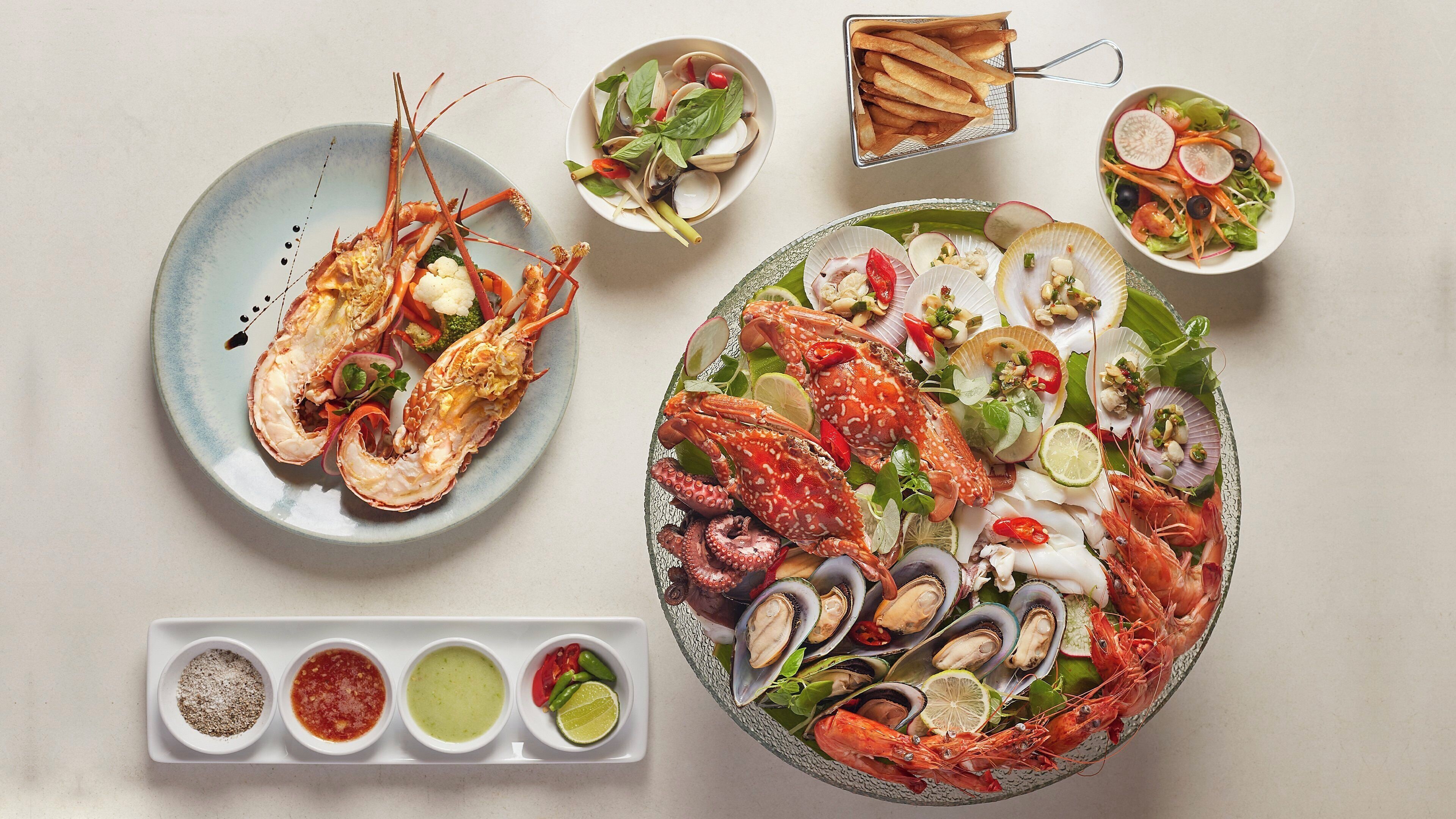A seafood platter with various shellfish and vegetables, accompanied by small bowls of condiments.