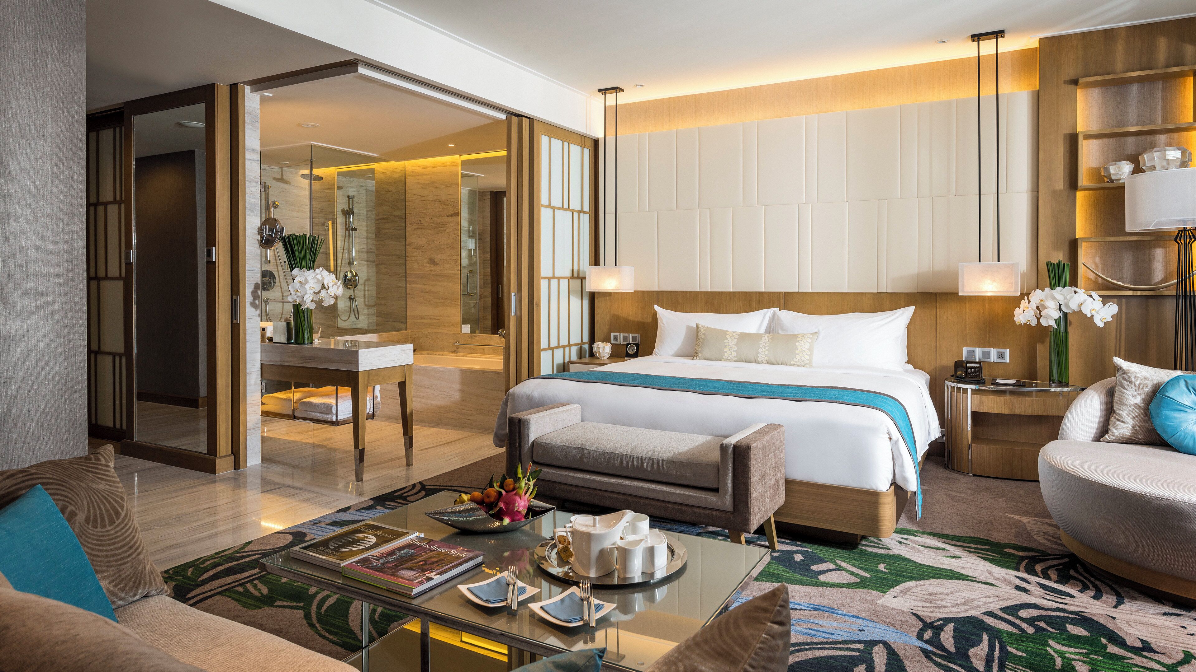 Een moderne hotelkamer met een groot bed, een zithoek, een glazen salontafel, en een badkamer met douche en spiegel.