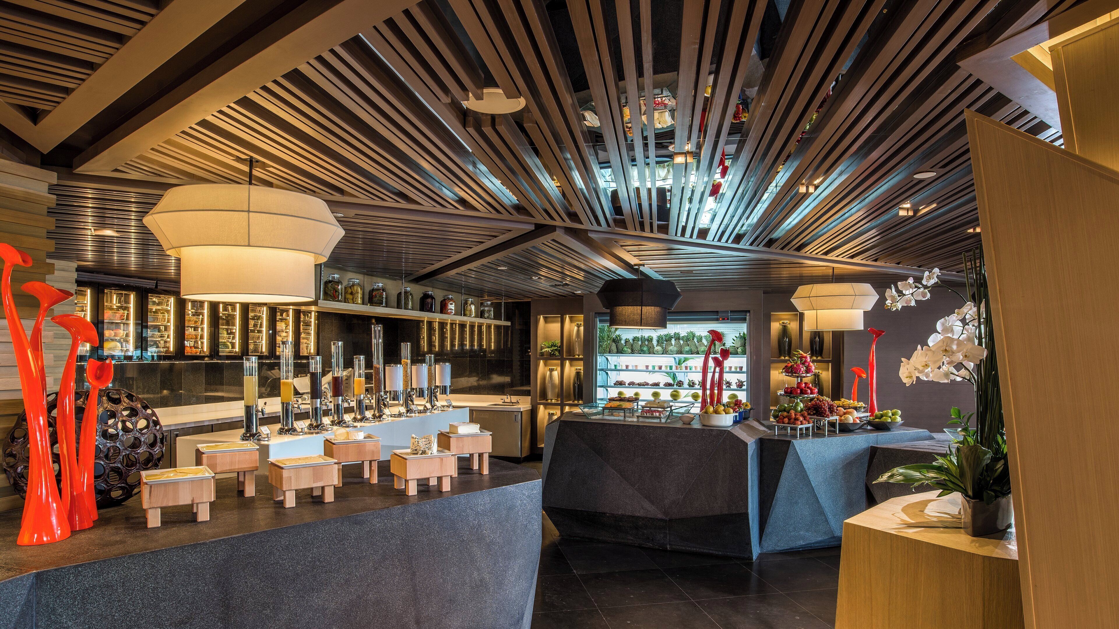 A modern bar area with a central counter, multiple stools, and a ceiling with linear light fixtures.