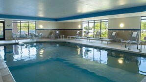 Ein Swimmingpool mit Liegestühlen und Sonnenterrassen, umgeben von großen Fenstern.