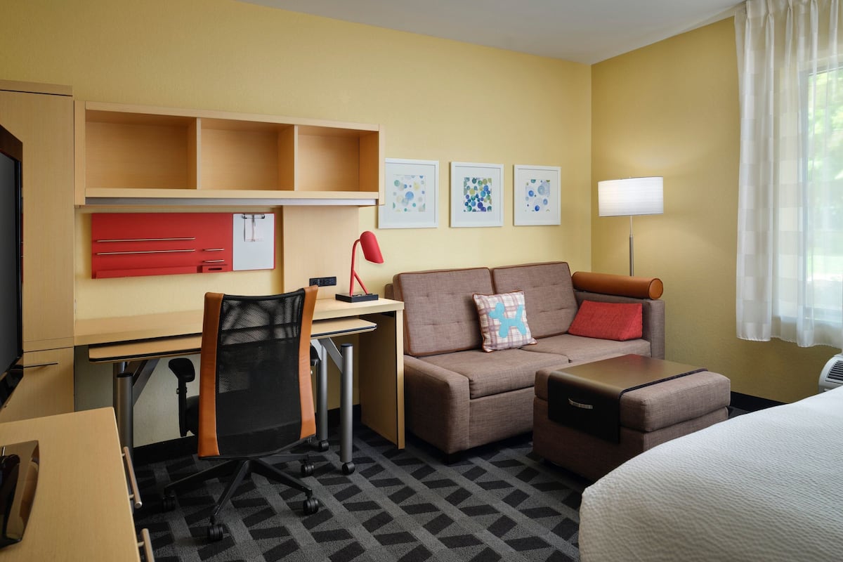Une chambre d’hôtel comprenant un lit, un canapé, un bureau avec une chaise, une télévision, une lampe et des œuvres d’art accrochées au mur.