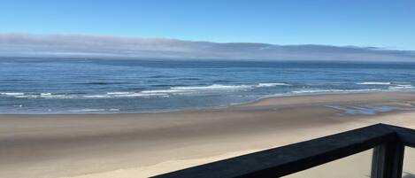 Una playa con olas, cielo despejado y una barandilla de madera.