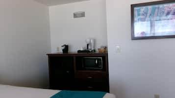 A hotel room with a bed, a microwave, a coffee maker, and a framed picture on the wall.