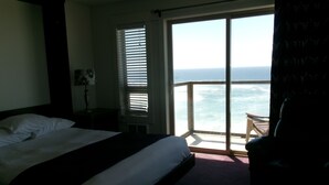 A hotel room with a bed, a chair, and a view of the ocean through large windows. - Seahorse Oceanfront Lodge (Lincoln City)