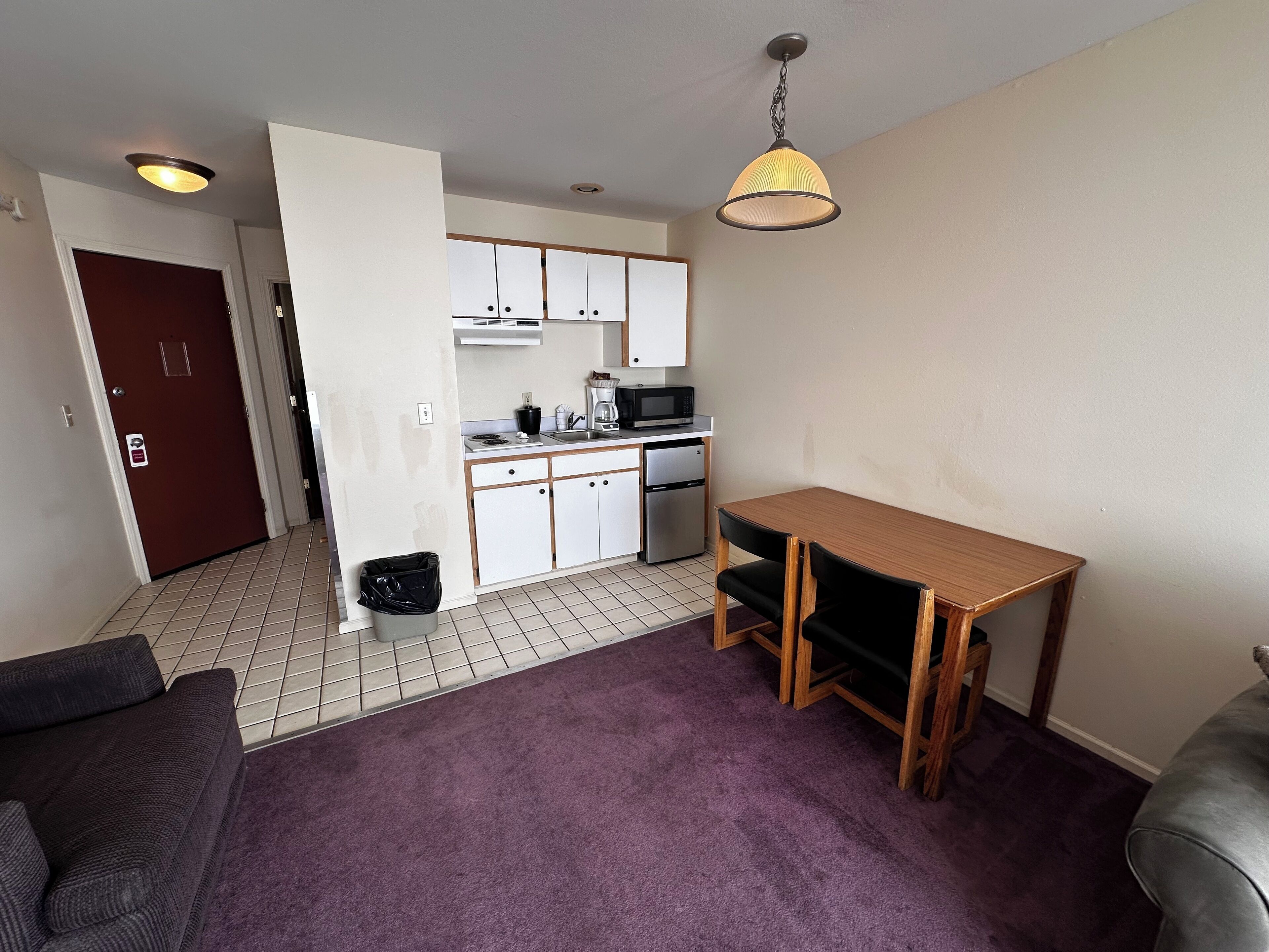 A compact living space with a kitchenette, a dining table, and a purple carpet.