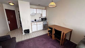 A compact living space with a kitchenette, a dining table, and a purple carpet.