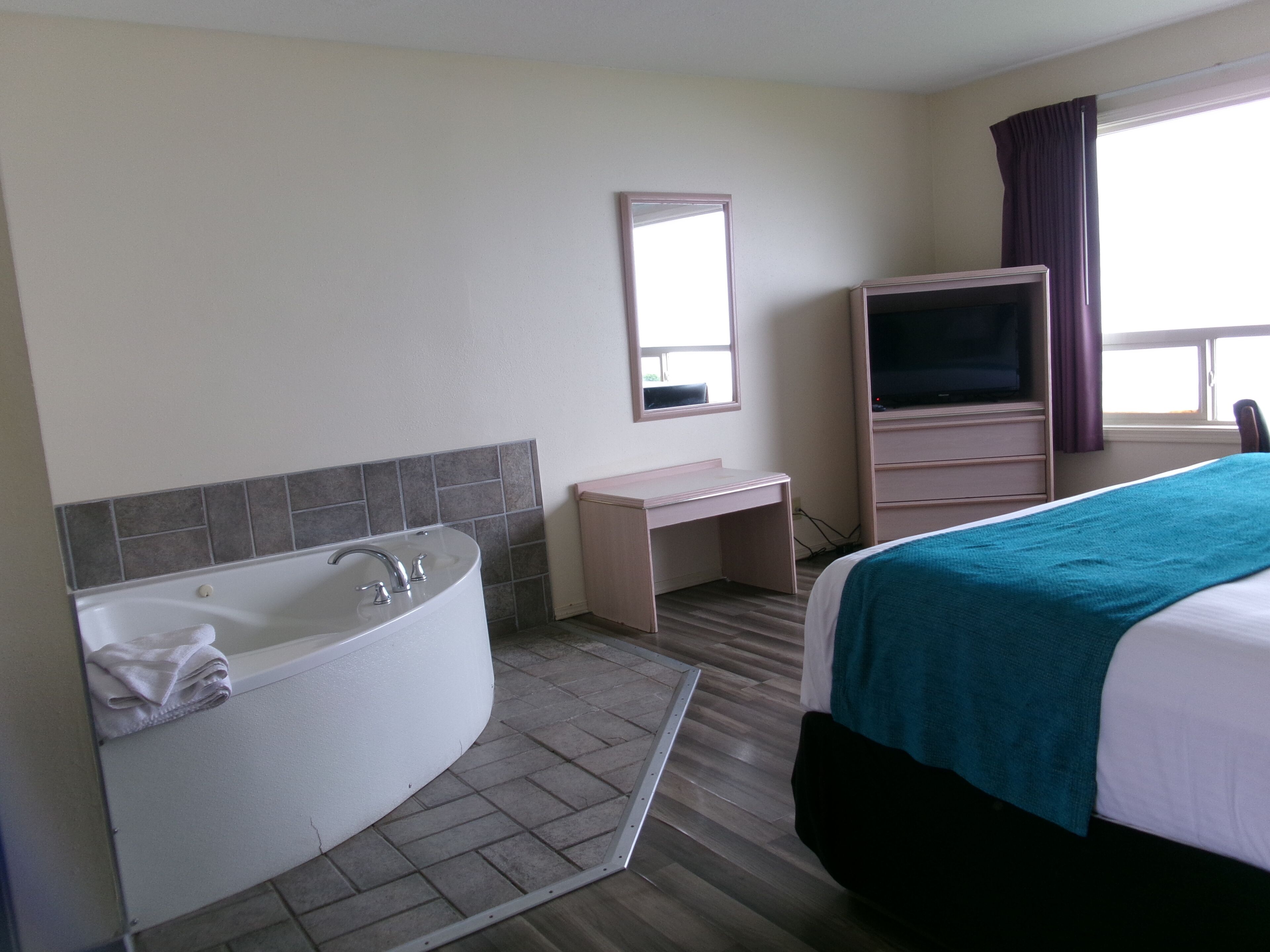 Una habitación de hotel con una cama grande, baño privado con bañera, escritorio y televisión.