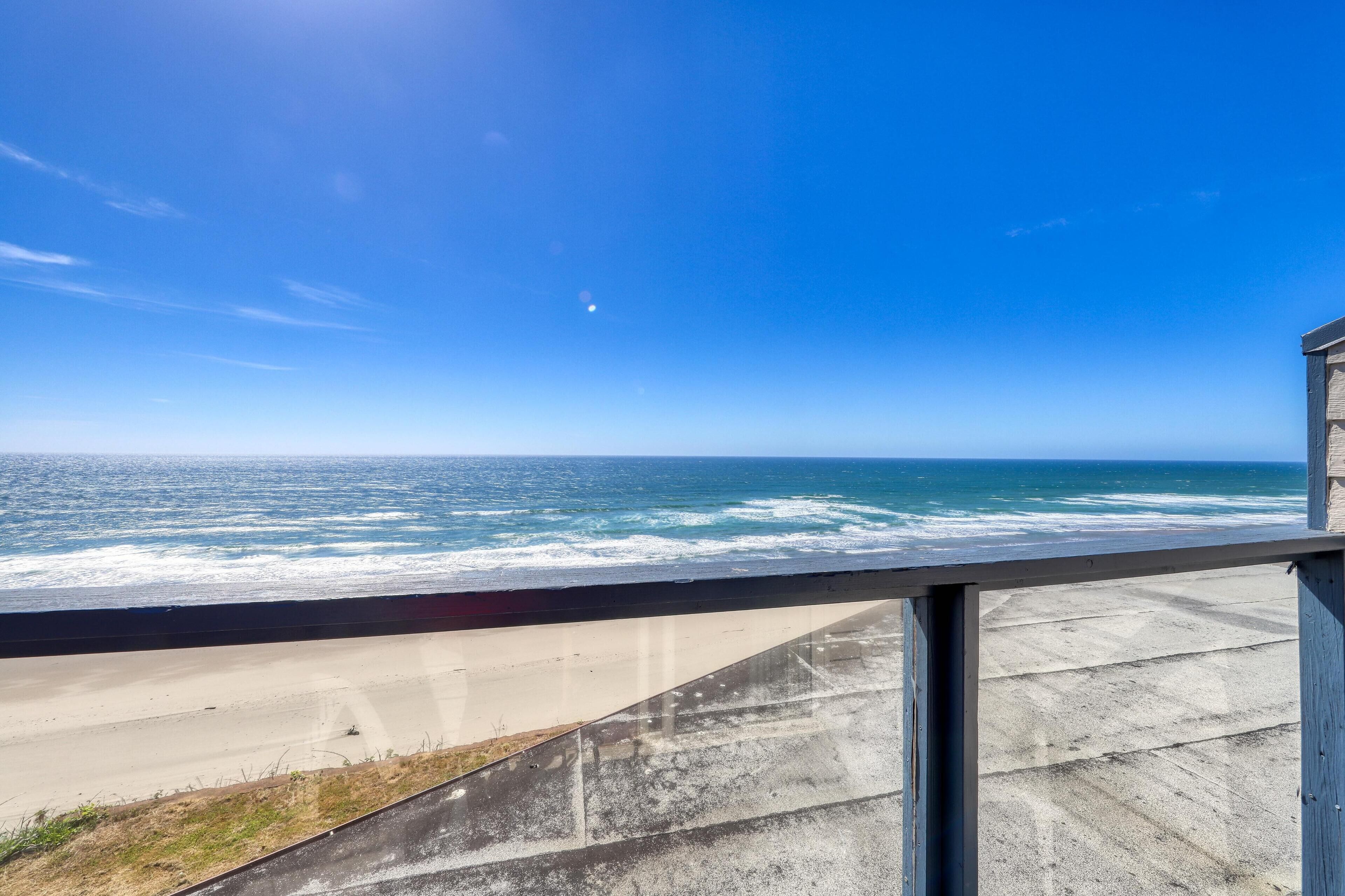 Vista costera desde un balcón, con cielo despejado, olas del océano y una playa de arena.