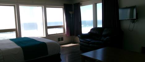 Quarto de hotel com cama, escrivaninha, cadeira e televisão.