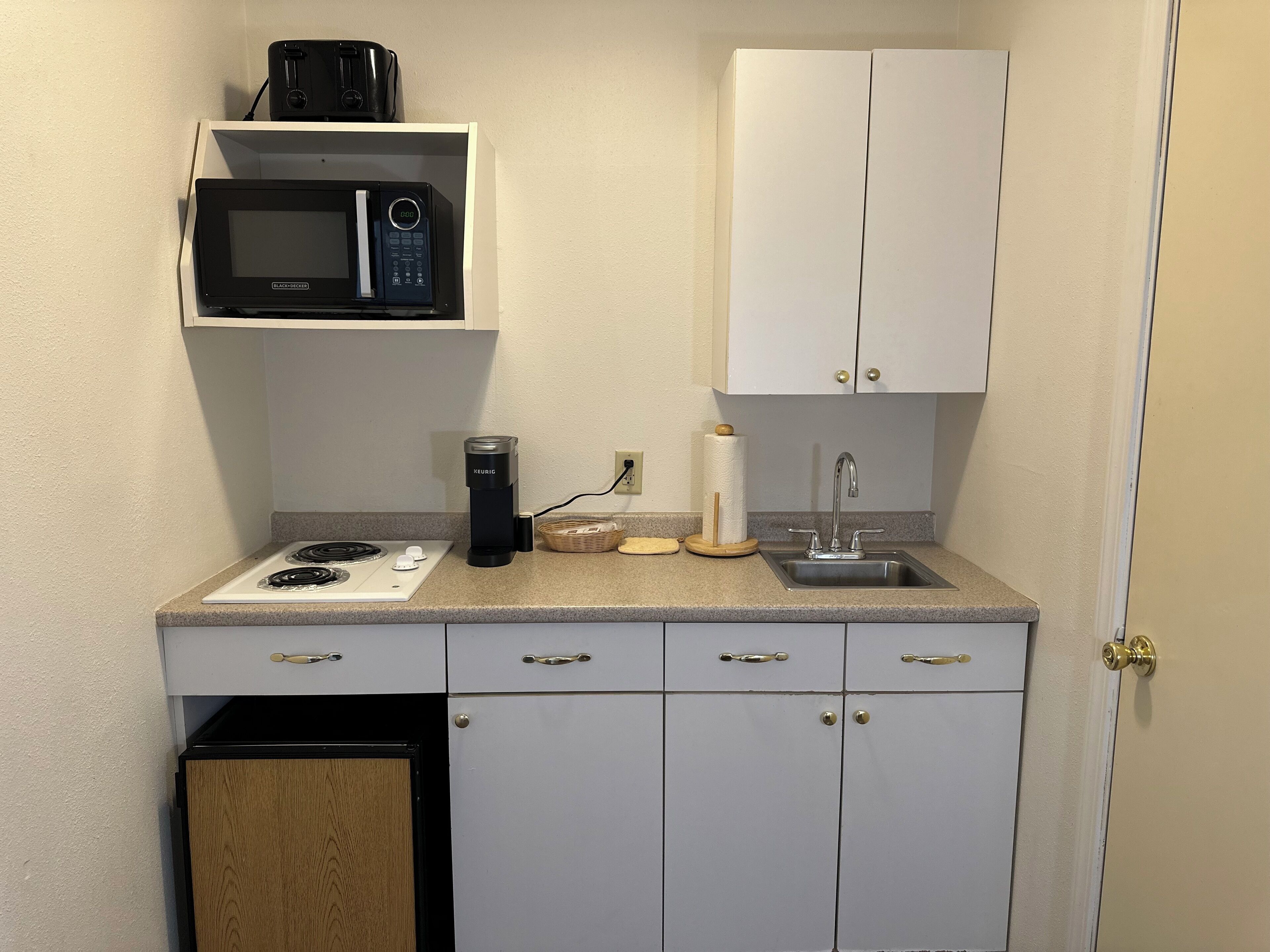 A compact kitchenette with a microwave, coffee maker, and a sink.