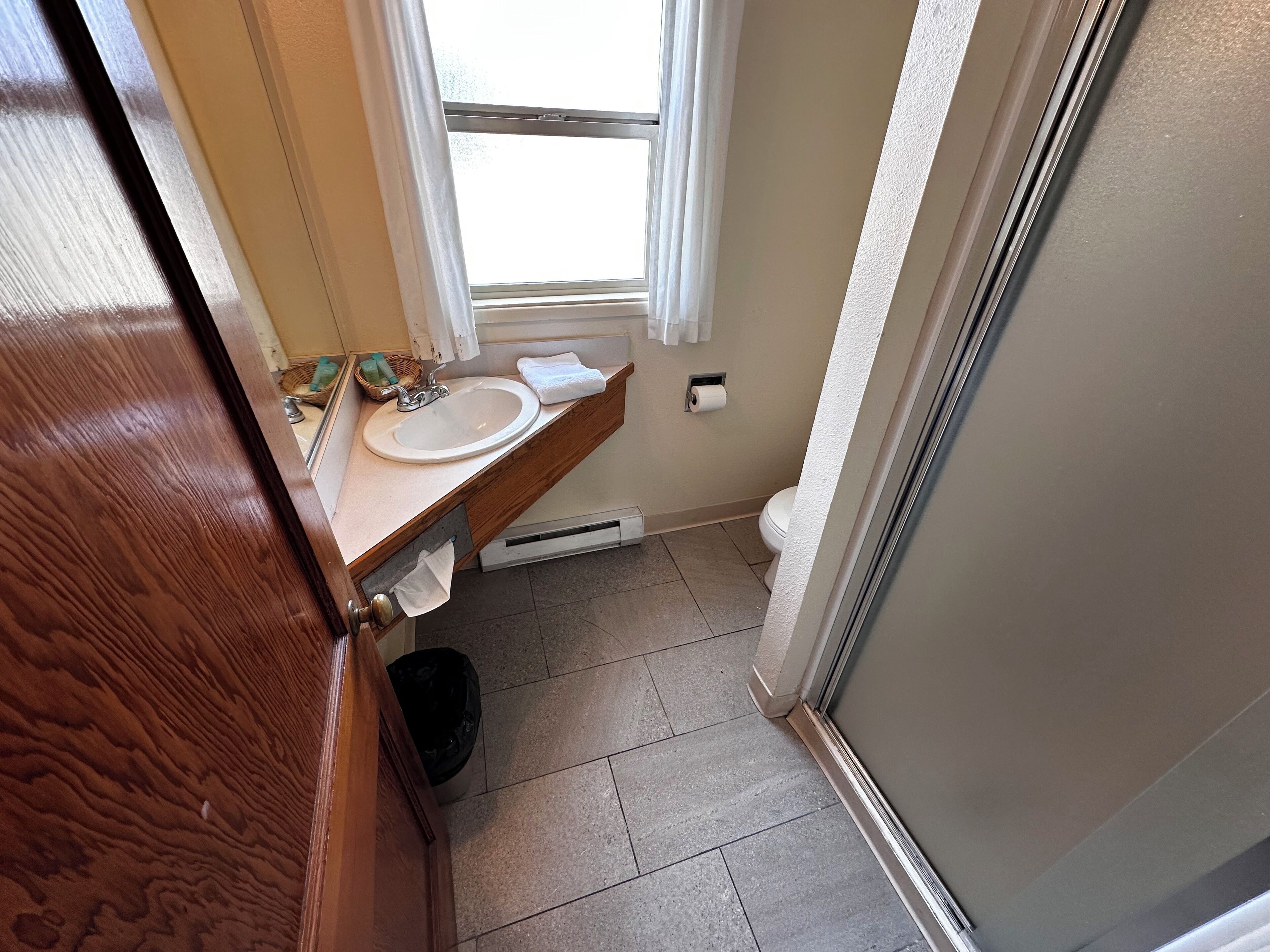A bathroom with a wooden vanity, a sink, a toilet, and a window.