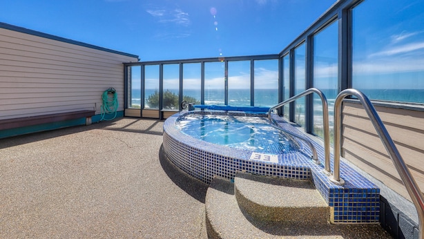 A hot tub with a view of the ocean, surrounded by glass walls and a concrete deck. - Seahorse Oceanfront Lodge (Lincoln City)