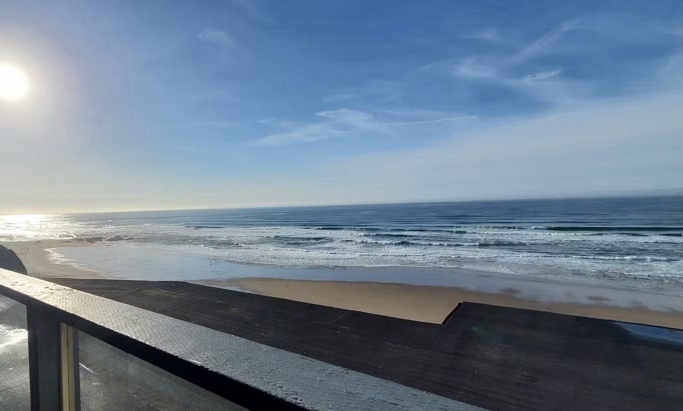 A beach with waves, a clear sky, and a sun setting or rising.