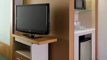 Habitación de hotel con televisor de pantalla plana sobre un soporte de madera, microondas sobre un estante blanco y mini refrigerador debajo.