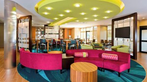 A modern lobby with a curved red sofa, wooden coffee table, and a yellow ceiling with recessed lighting. - SpringHill Suites by Marriott Philadelphia Langhorne (Langhorne)