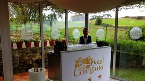 Zona de recepción con un cartel que dice "Hotel Collegiata" y vistas a un campo de golf a través de amplias ventanas.