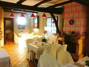 Un comedor con mesas dispuestas para comensales, chimenea y lámparas colgantes rojas.