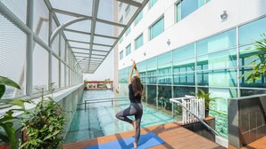 Une femme pratiquant le yoga sur un tapis bleu dans un espace intérieur doté d’une piscine et présentant une architecture moderne.