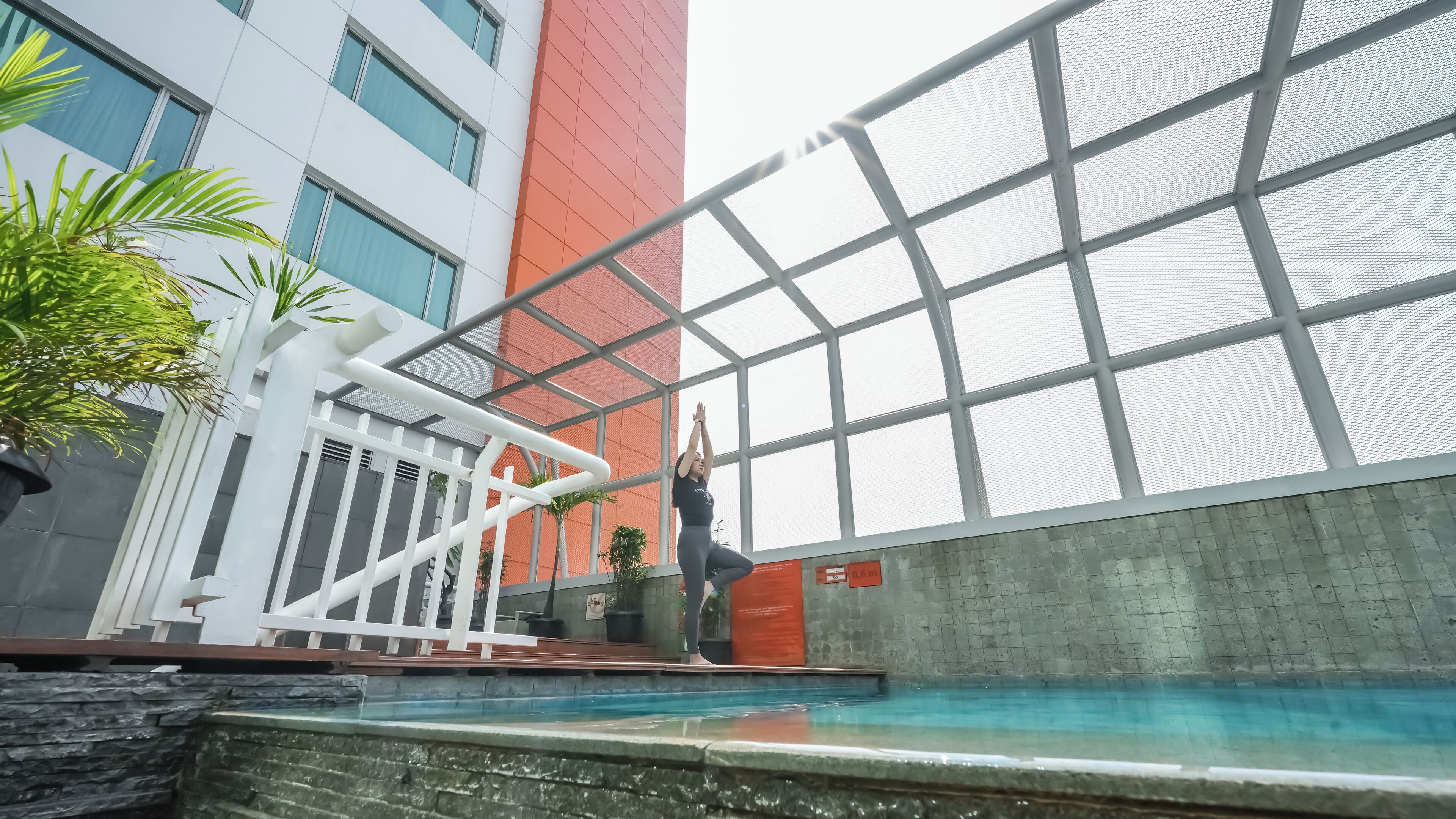 A modern indoor pool area with a glass enclosure, a white railing, and a stone wall.