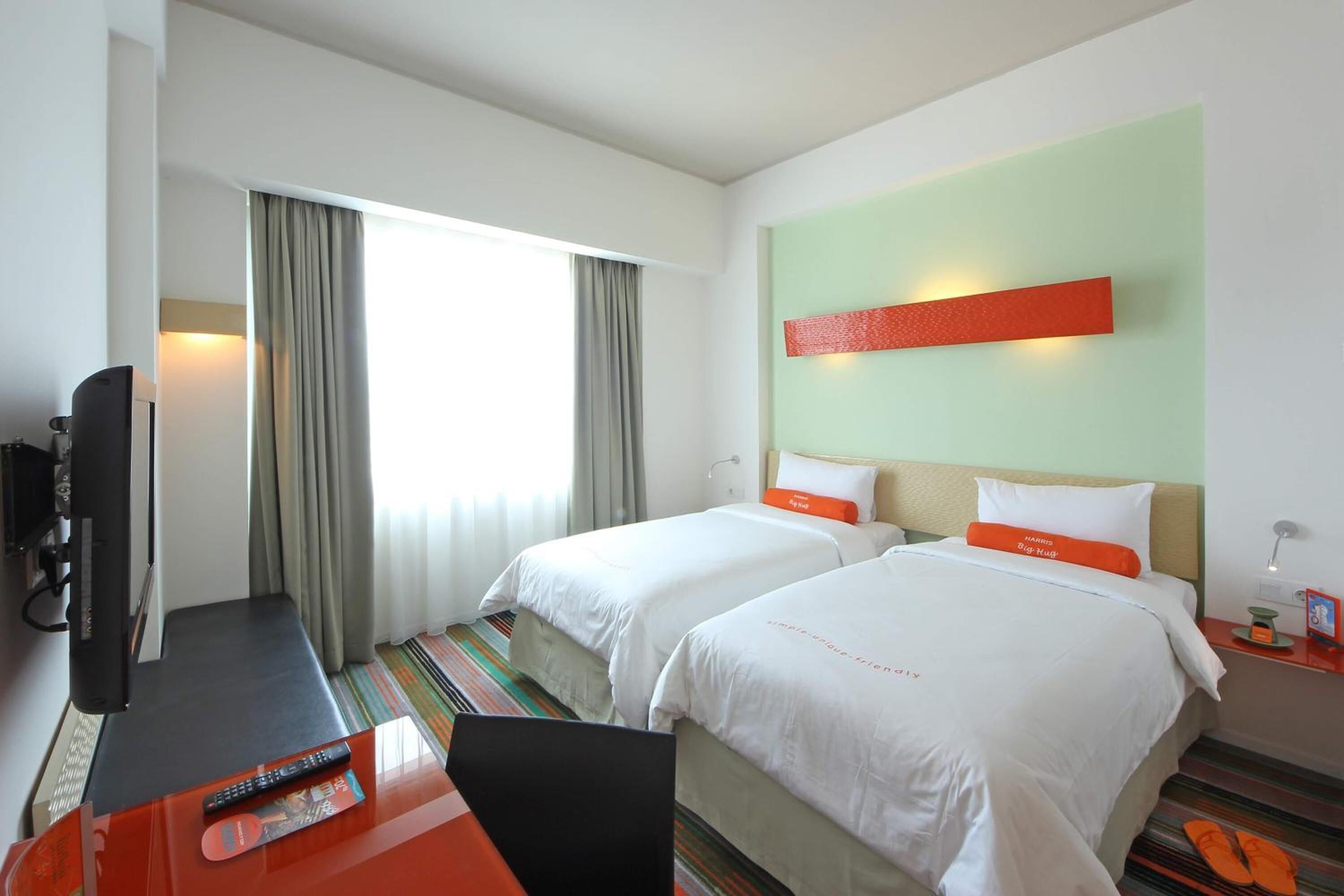 Une chambre d’hôtel avec deux lits, un bureau avec un ordinateur portable, une télévision et une fenêtre avec des rideaux.