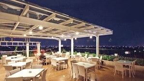 Un espace de restauration en plein air avec des tables et des chaises, un plafond en verre et une vue sur la ville la nuit.