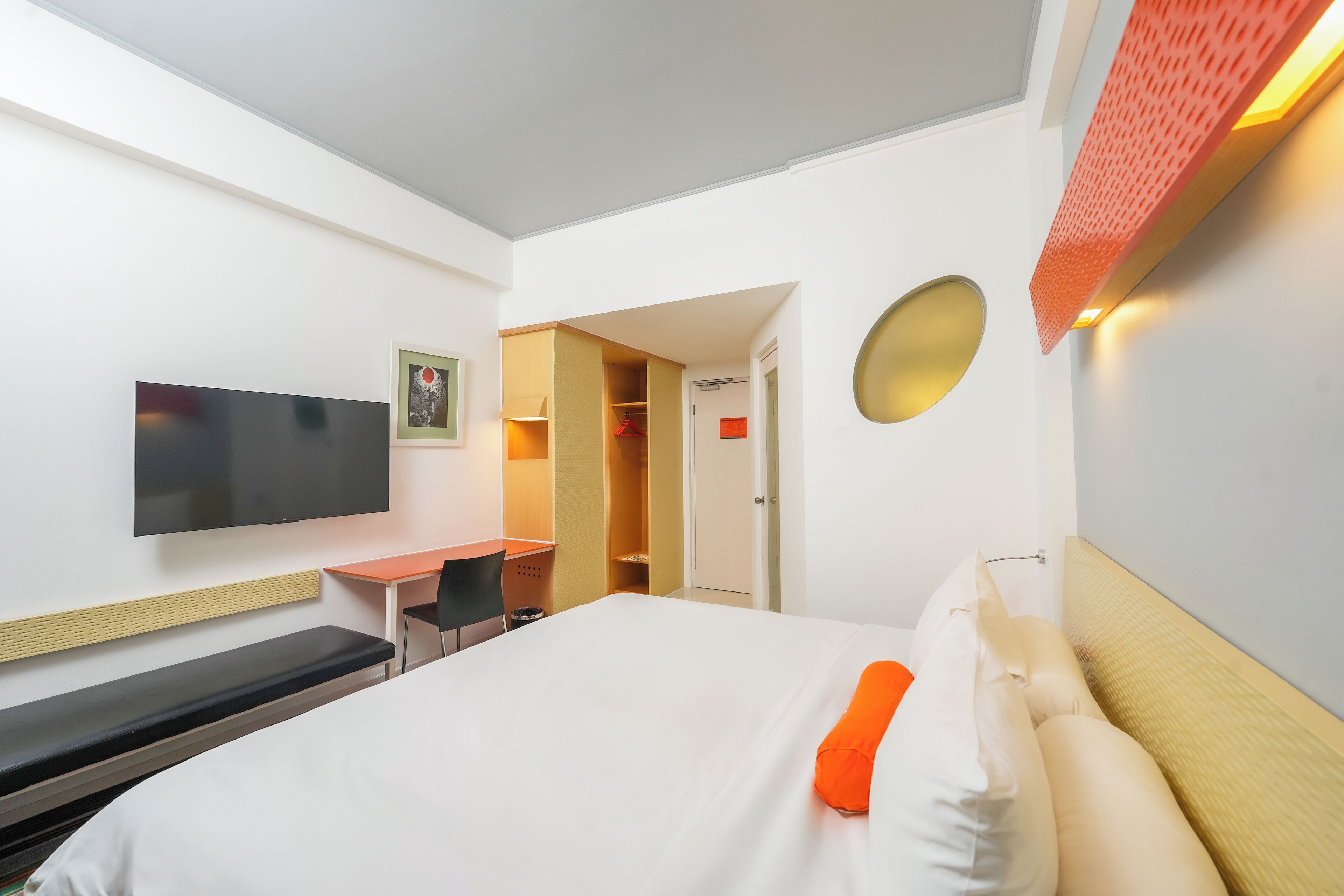 A hotel room with a bed, a desk, a chair, a TV, and a wardrobe.