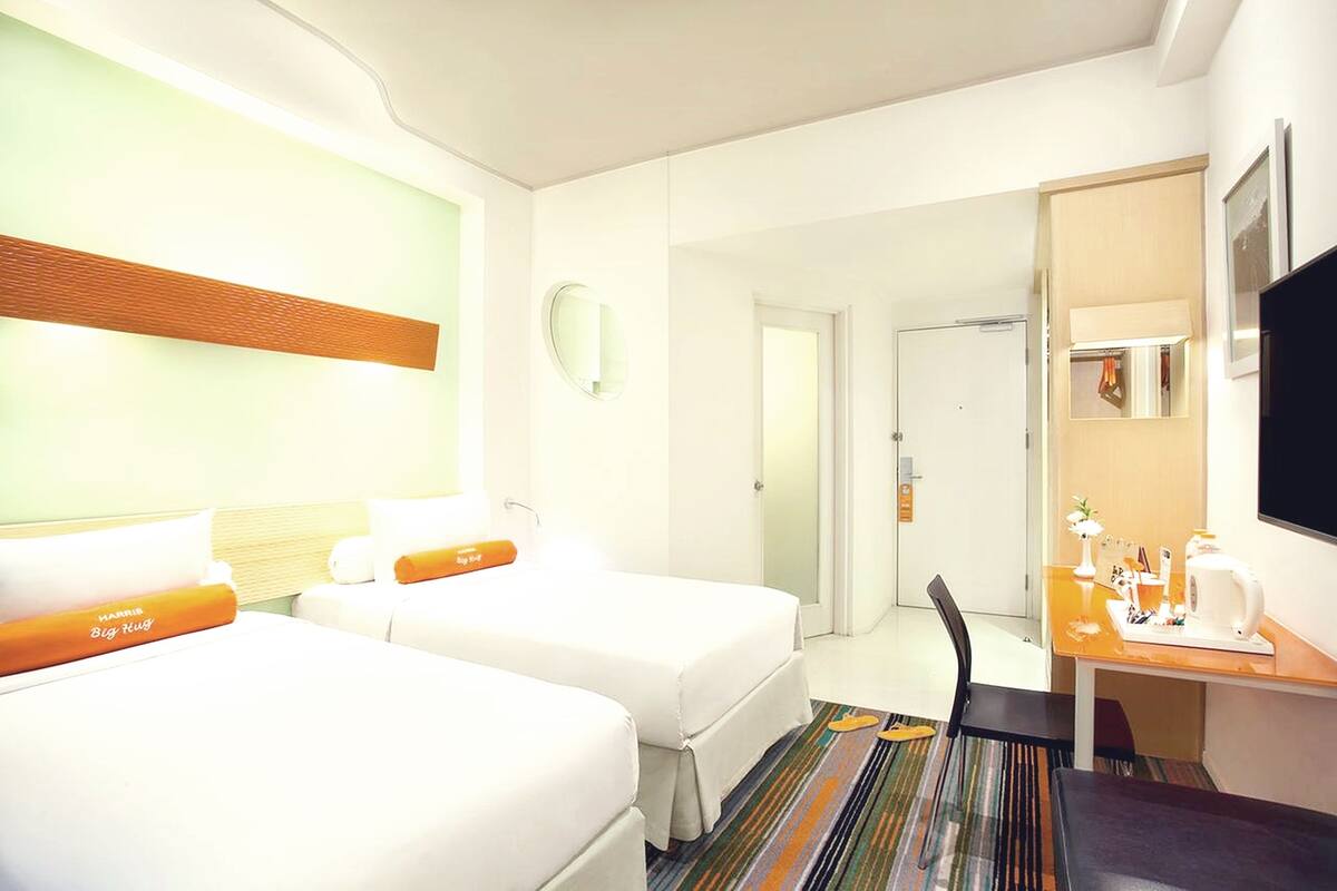 Habitación de hotel con dos camas, un escritorio con silla, televisor y baño visible a través de una puerta abierta.