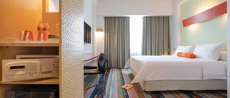 Una habitación de hotel con una cama, un escritorio con microondas, una silla y una alfombra a rayas.