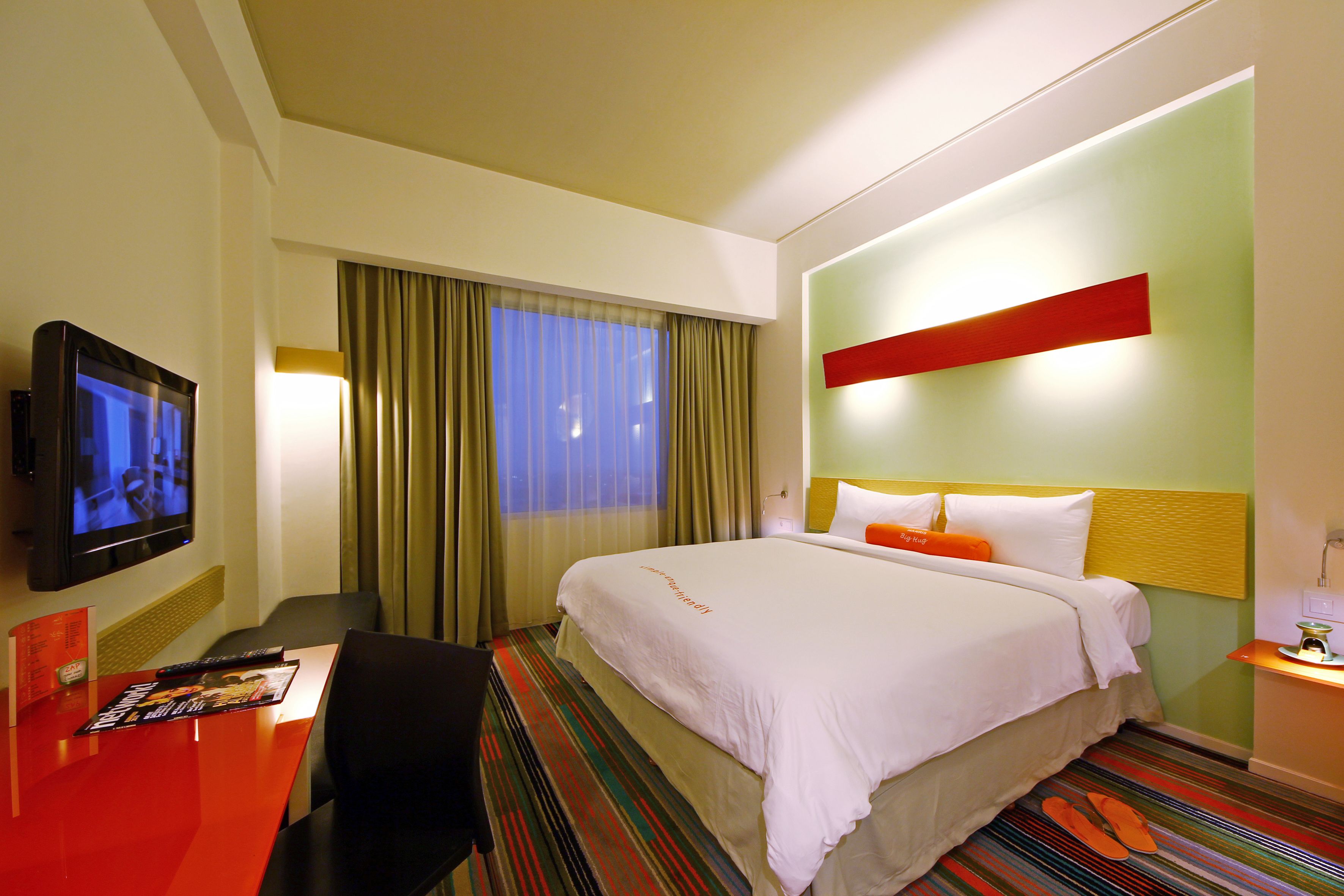 Una habitación de hotel con cama, televisión, escritorio y ventana con cortinas.