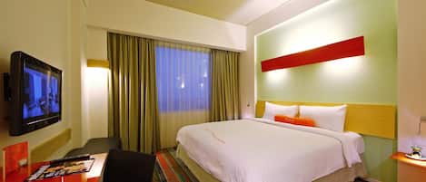 Una habitación de hotel con cama, televisión, escritorio y ventana con cortinas.